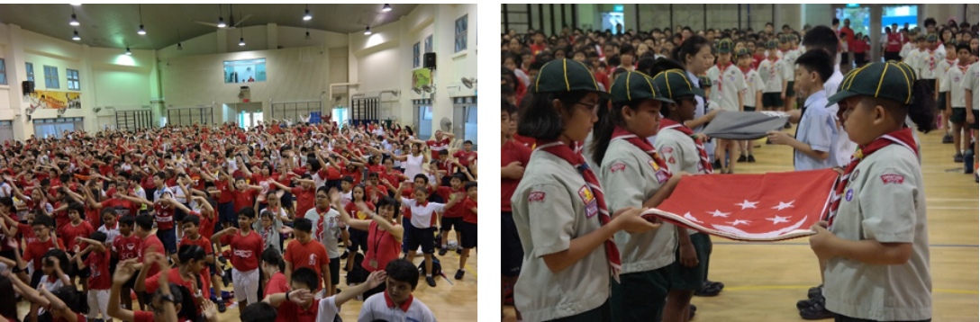Scouts in uniform hold a red flag with stars indoors, while a large crowd of students in red gather in a hall.